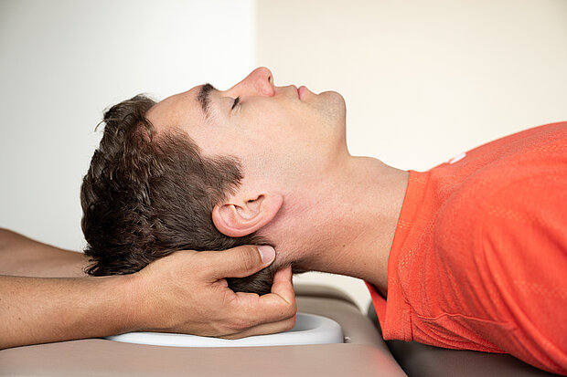 Osteopath stützt den Hinterkopf eines Patienten während einer kranio-sakralen Behandlung 