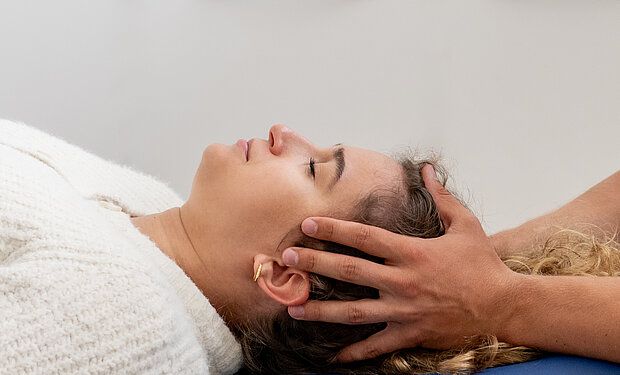 osteopathische Behandlung durch kranio-sakrale Therapie am Kopf des liegenden Patienten