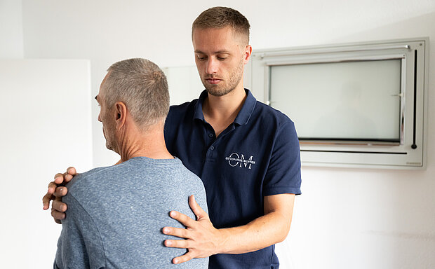 Osteopath in Maintal untersucht die Wirbelsäule eines sitzenden Patienten